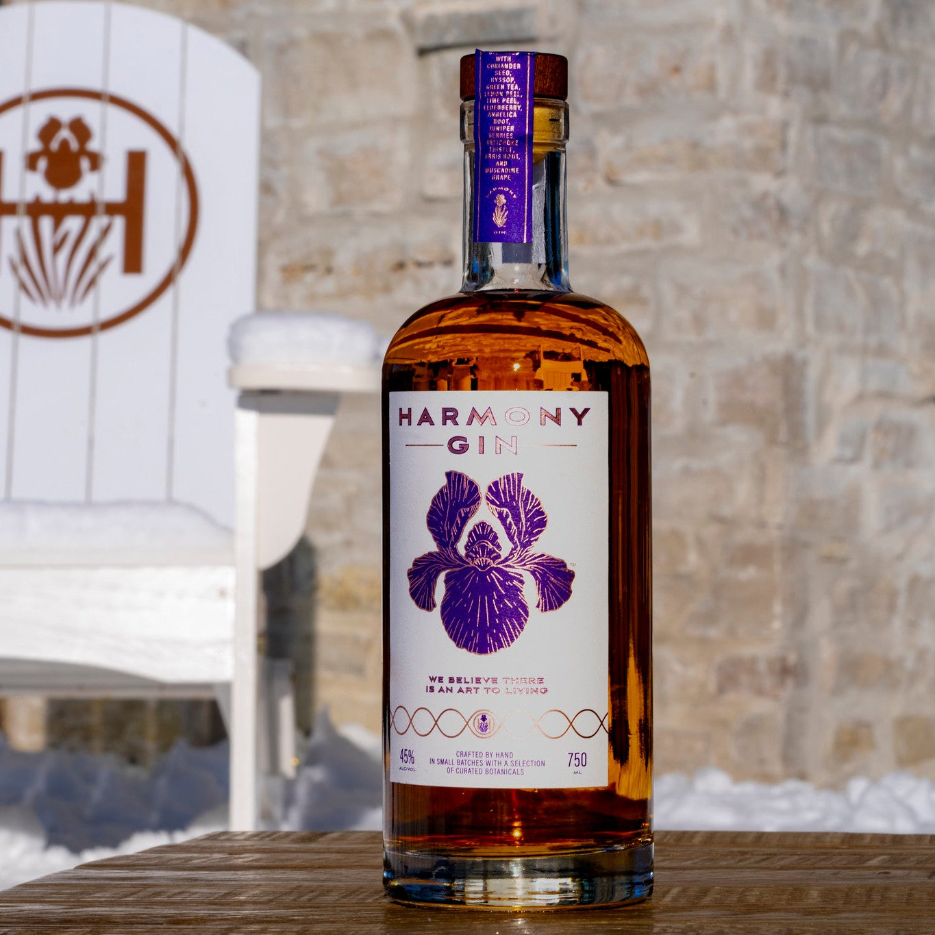 Bottle of Harmony Gin on a wooden surface with a white chair and stone wall in the background.